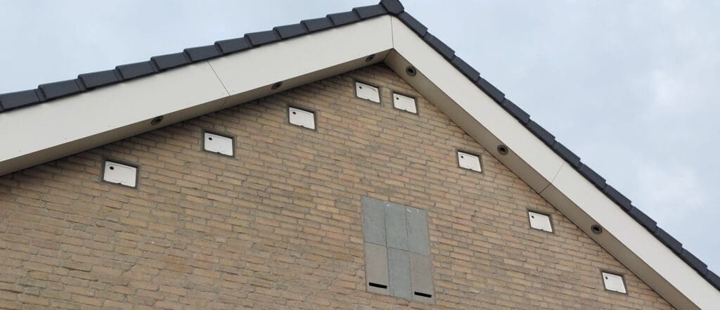 Bovenste gedeelte van zijgevel huis van onderaf gezien, met daarin witte vierkantje langs de schuine randen