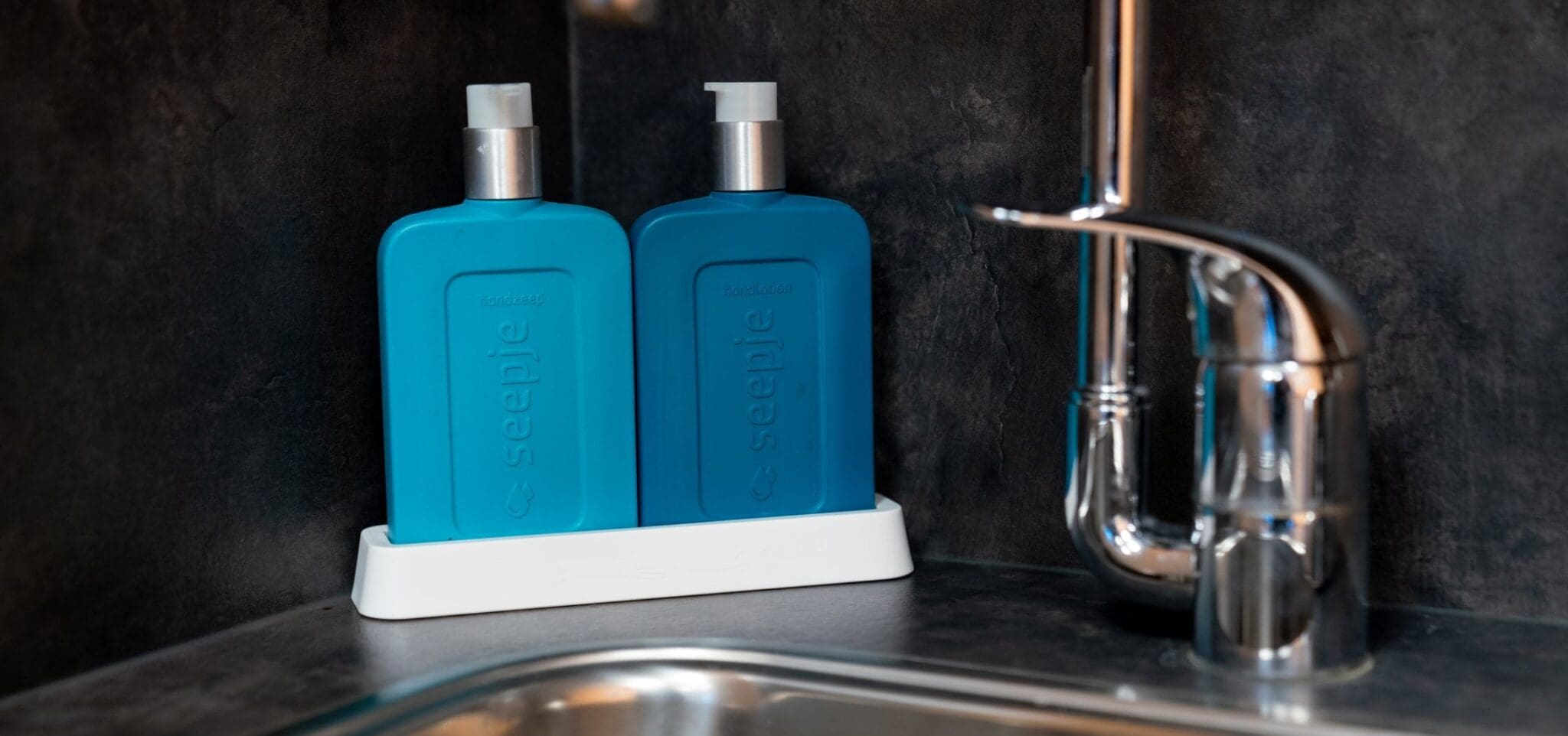 close-up van kraan bij moderne wasbak, met 2 blauwe zeep-dispensers