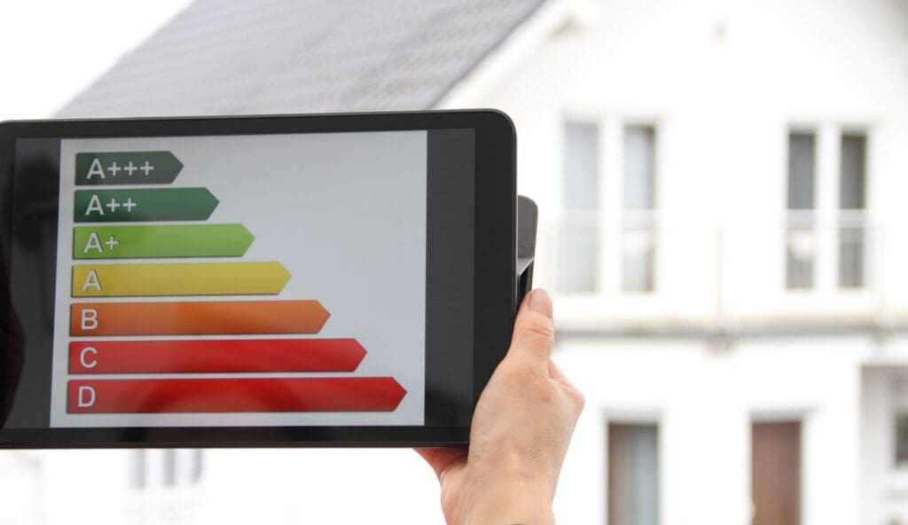 hand houdt tablet vast met daarop de trap van energielabels. op de achtergrond een wit woonhuis