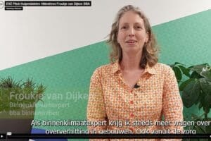 Screenshot uit een video. Iemand staat voor een muur met deels groen behang, deels wit. Kijkt recht in de camera. Plant op achtergrond en op tafeltje naast persoon. Tekst onder in beeld.